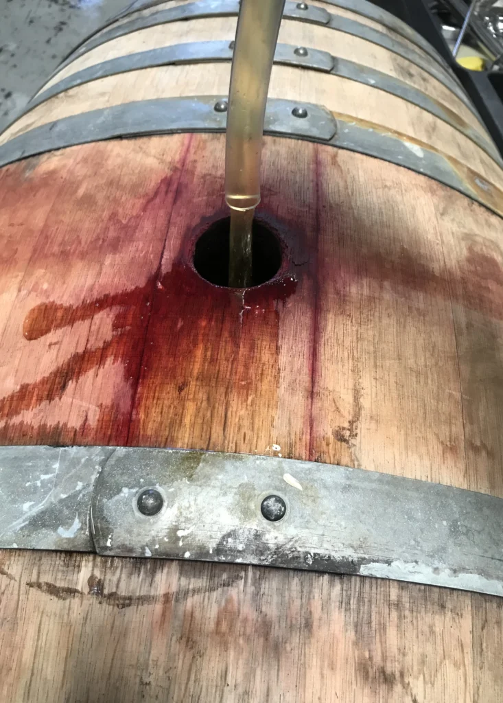 An oak barrel being filled through the bung hole, the wood stained dark around it.